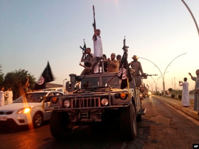 FILE - Fighters from the Islamic State group parade in a commandeered Iraqi security forces armored vehicle down a main road at the northern city of Mosul, Iraq.