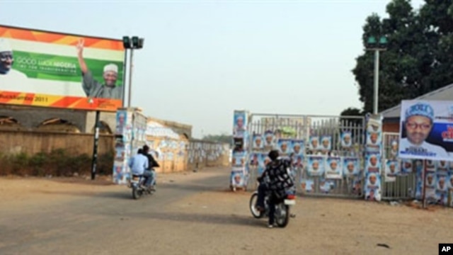 Members of the Party Loyalists drive their motocycles outside the entrance of a park in front of posters  featuring  Nigeria's opposition leader Mohammadu Buhari (R) and Nigeria's President Goodluck Jonathan and his Vice President Namadi Sambo (L)  in Kad