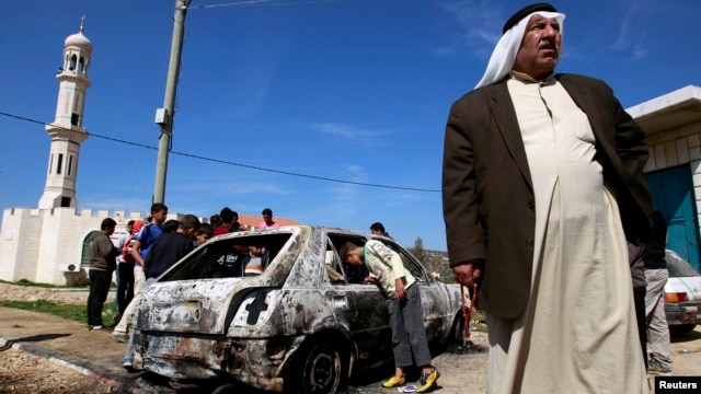 A Palestinian stands near a burnt car in the West Bank village of Kusra, near Nablus, February 21, 2013.