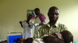 Savio Niwagaba holds his newborn baby as his wife Chrisente, behind him, has a contraceptive implant inserted in her arm, Kanungu, Uganda, June 19, 2012. (VOA / Hilary Heuler)