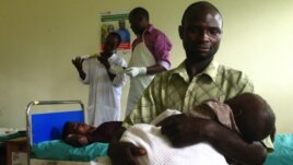 Savio Niwagaba of Uganda holds his newborn baby as his wife Chrisente, behind him, has a contraceptive implant placed in her arm