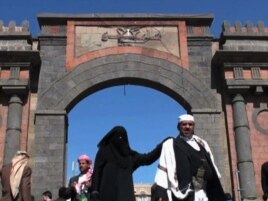 A woman walks past a fortified gate in Sanaa
