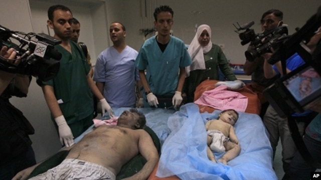 Libyan doctors stand near bodies of a man and a baby found in the damaged residential building in Tripoli's outskirts, Libya, on Sunday, June 19, 2011. Libyan officials claimed that the building was hit by a NATO airstrike. NATO continued to strike target