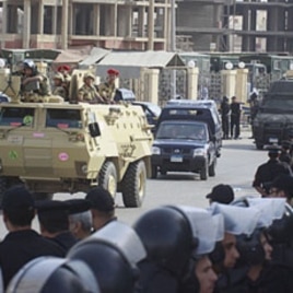 Egyptian policemen line the street as an armored army vehicle guards a convoy carrying former Egyptian interior minister Habib el-Adly and his aides, as they arrive at the court in Cairo, May 21, 2011
