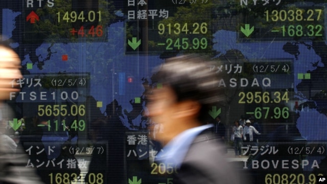 Hombres de negocios caminan frente a la pizarra electrónica de una firma de inversiones, en Tokio. El Fondo Monetario Internacional ha reducido las perspectivas globales de crecimiento.