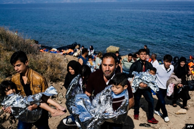 Men carry their children wrapped in emergency blankets shortly after arriving with other migrants and refugees on the Greek island of Lesbos after crossing the Aegean sea from Turkey, Oct. 18, 2015.