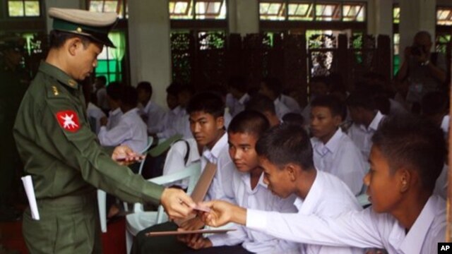 A Burma soldier (L) gives the national identity card to child soldiers who were recruited into the army before reaching the age of 18, during a ceremony where they were handed over to their parents and guardians in Rangoon, September 3, 2012.