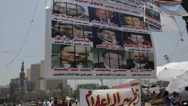 Egyptian protesters walk under a big banner with pictures of some journalists. It reads 'The military council protects the former regime.' Another banner calls for 'Media purification,' Tahrir Square, Cairo, Egypt, July 10, 2011