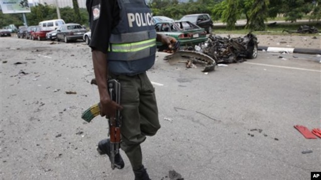 A Nigerian police officer walks past the burnt out shell of a car, after a car bomb exploded in Abuja, Nigeria, 1 Oct  2010