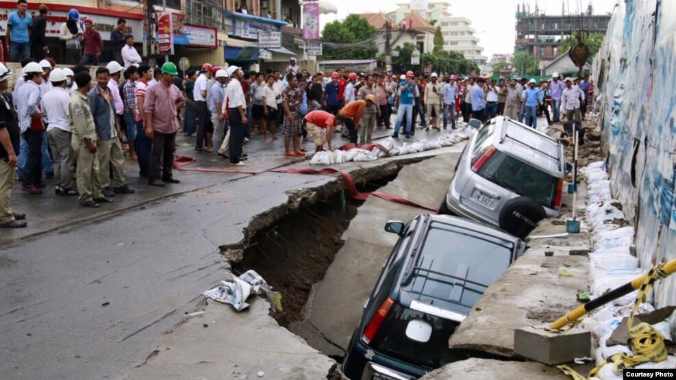 ​​Onlookers watch the cars sink in a hole by a construction site by Phnom Penh's Olympic Stadium after a heavy rain on Wednesday, June 8, 2016. (Courtesy of SBN)