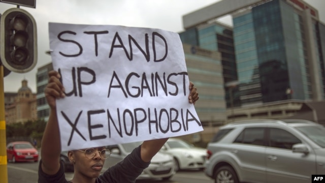 A South African holds a sign as she stands on the side od a road in Sandton, as xenophobic violence continued, on April 18, 2015.
