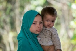 在泰国-马来西亚边界被拘留的一个疑似来自新疆的维吾尔人抱着一个孩子在临时收容所里（2014年3月14日）