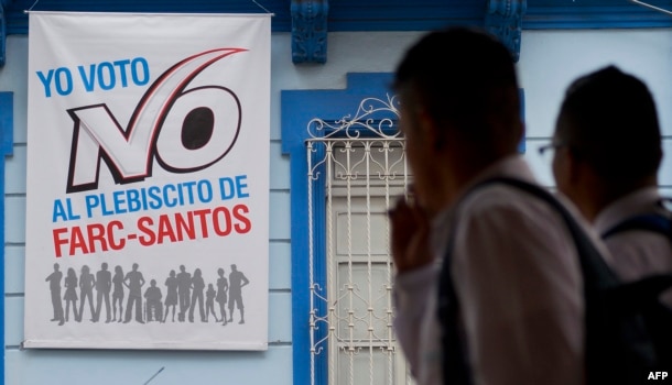 FILE - People walk by a placard that reads: "I vote NO the plebiscite FARC-Santos" in support of the "NO" in the upcoming referendum on the peace agreement in Cali, Colombia, Sept. 30, 2016.