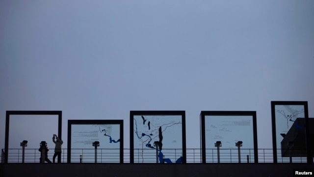A tourist looks toward the north through a binoculars as another takes pictures at Imjingak Pavilion near the demilitarized zone (DMZ), which separates the two Koreas, in Paju, north of Seoul, March 14, 2013. 