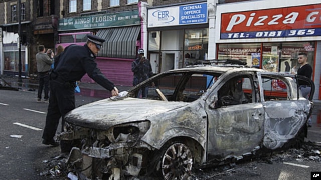 A police officer removes identification from a police car set on fire and burnt during riots in Tottenham, north London, August 7, 2011