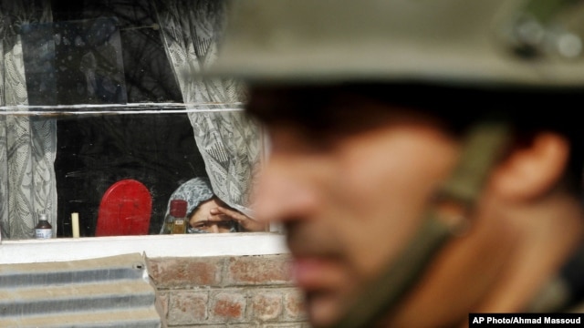 A Kashmiri woman watches from inside her home window an Indian policeman stand guard during a protest on the outskirts of Srinagar, India, Jan. 8, 2013.