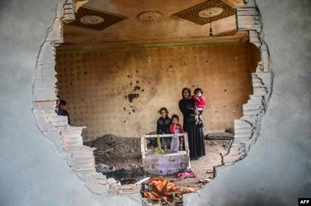 FILE - A women and her children stand in the ruins of battle-damaged house in the Kurdish town of Silopi, in southeastern Turkey, near the border with Iraq on January 19, 2016.