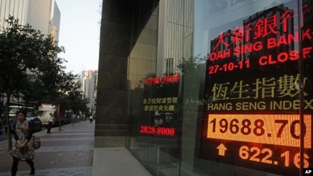 A woman walks past a screen displaying the Hang Seng stock index in Hong Kong, October 27, 2011.