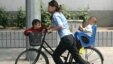 一位中国女子前后带着孩子推着自行车