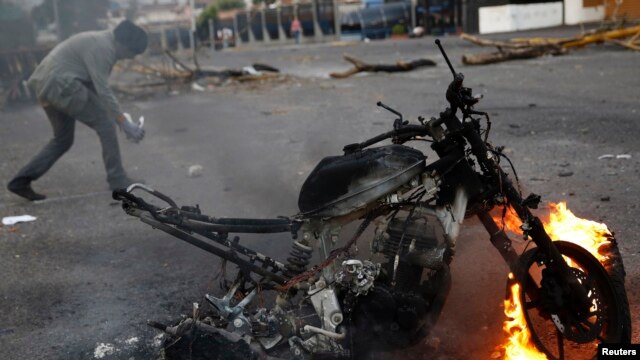 Một người biểu tình chống chính phủ đi qua một chiếc xe máy bị đốt sau một cuộc biểu tình ở San Cristobal,Venezuela, 27/2/2014. 