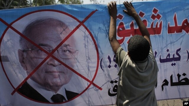 An Egyptian youth hangs a banner with a defaced picture of presidential candidate, Ahmed Shafiq and Arabic that reads "Shafiq, the former regime," during a protest in front the Supreme Constitutional Court in Cairo, Egypt, June 14, 2012.