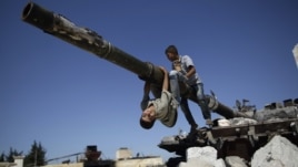A boy looks back while he and another boy play on a Syrian military tank, destroyed during fighting with the Rebels, in the Syrian town of Azaz, on the outskirts of Aleppo, Sunday, Sept. 2, 2012.