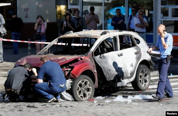 FILE - Investigators inspect a damaged car at the site where journalist Pavel Sheremet was killed by a car bomb in central Kiev, Ukraine, July 20, 2016.