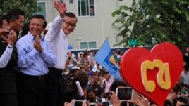 Opposition Cambodia National Rescue Party (CNRP) leader Sam Rainsy, right, accompanied by his party's Vice President Kem Sokha, second from right, waves to his party supporters during a public forum of the July 28 election result, in Phnom Penh, Cambodia, Monday, Aug. 26, 2013. Rainsy told thousands of supporters that his party will stage massive protests unless an independent committee begins investigating alleged irregularities in last month's election. (AP Photo/Heng Sinith)