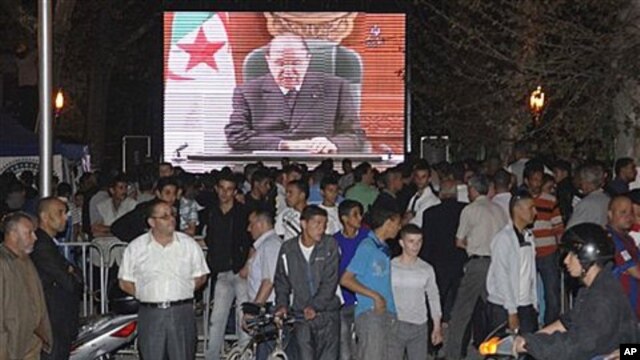 People congregate around a large TV screen  showing Algeria's President Abdelaziz Bouteflika in Algiers, April 15, 2011