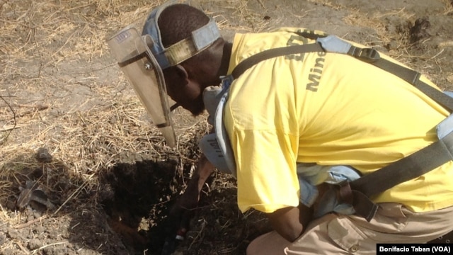 Cons Wani, who works with the Danish Demining Group, brushes dirt away to reveal a rocket-propelled grenade that was found in the center of Bentiu, in South Sudan. (VOA/Bonifacio Taban)