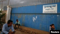 FILE - People wait for garment workers to leave a factory in a suburb of Phnom Penh.