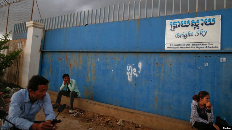 FILE - People wait for garment workers to leave a factory in a suburb of Phnom Penh.