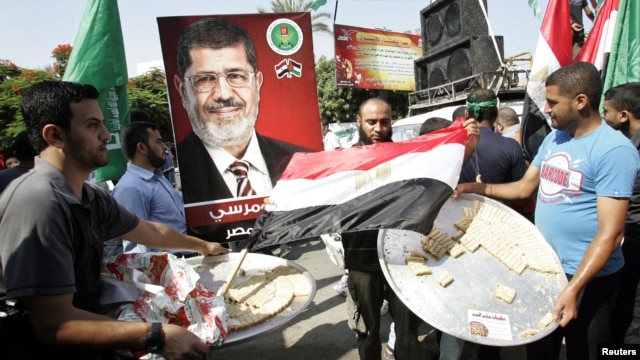 Palestinians carry trays of sweets and an Egyptian flag (C) in front of a placard depicting Egypt's Muslim Brotherhood's presidential candidate Mohamed Morsi in Gaza City, June 18, 2012.