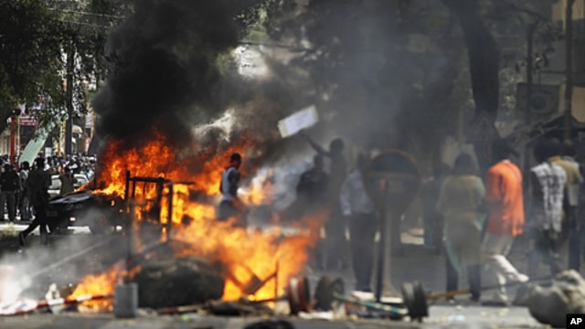 Anti-government protesters walk past a burning vehicle and barricades during a demonstration in the capital Dakar, June 23, 2011