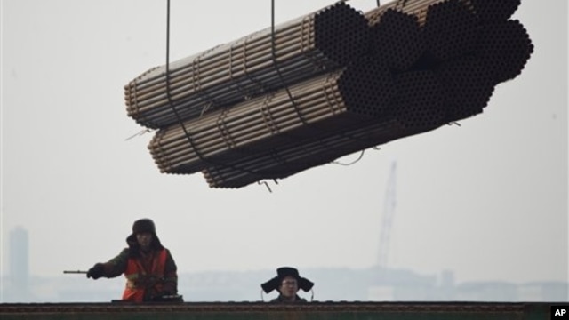 Port workers watch as steel pipes are unloaded from freighter at Cao Feidian Port, Tangshan, Hebei province, China, Feb. 20, 2012.