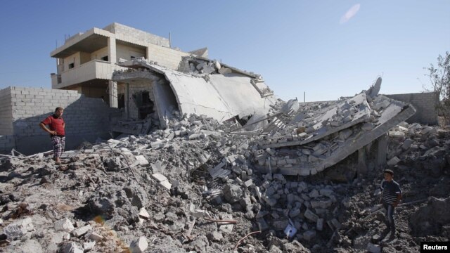 Civilians stand near a destroyed house in wake of early morning Syrian Air Force strikes, Aziz, Sept. 3, 2012.