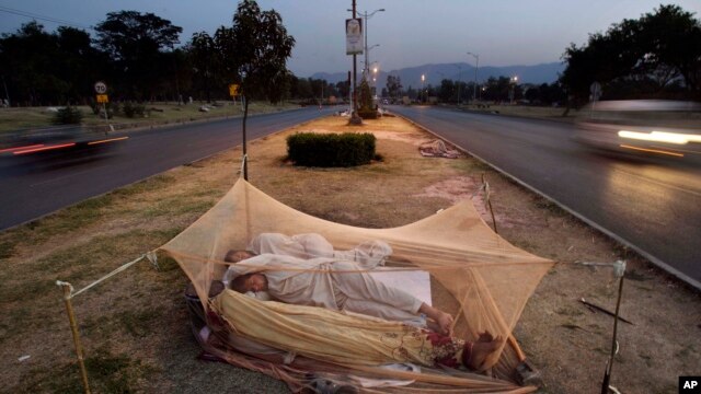 FILE - Vehicles move past Pakistani day laborers sleeping under a mosquito net in the middle of a road in Islamabad, Pakistan.