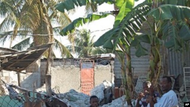 A family in the destroyed town of Carrefour, Haiti sits amid the charred rubble of their home, 25 Jan 2010