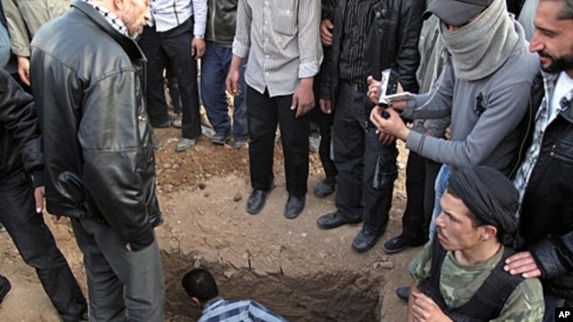 A Free Syrian Army fighter sits next to the grave of a comrade during the funeral for four people killed in a raid by government forces in a neighborhood of Damascus, Syria, April 5, 2012.