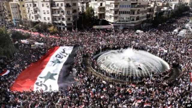Pro-Syrian regime protesters, carry a giant Syrian flag during a demonstration against the Arab League decision to suspend Syria, in Damascus, Syria, November 13, 2011.