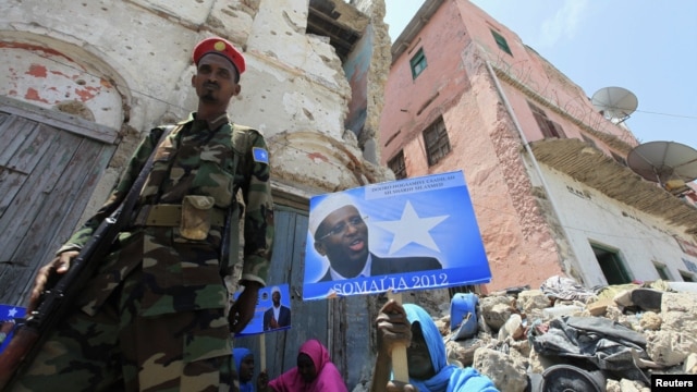 Wani sojan gwamnatin Somaliya yana wucewa a kusa da wata mace rike da kwalin fasta na yakin neman zaben shugaba Sheikh Sharif Ahmed