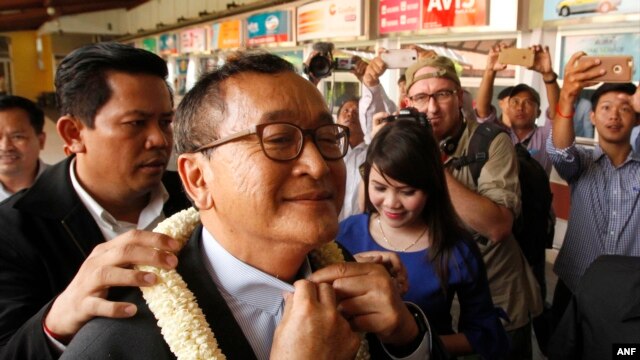 FILE - Sam Rainsy, foreground, leader of the opposition Cambodia National Rescue Party (CNRP), receives a garland of jasmine upon his arrival at Phnom Penh International Airport in Phnom Penh, Cambodia, Aug. 16, 2015.