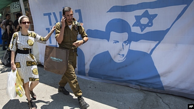 An Israeli soldier and a woman walk past a protest tent calling for the release of captured Israeli soldier Gilad Schalit, near the Prime Minister's residence, in Jerusalem, June 24, 2011.