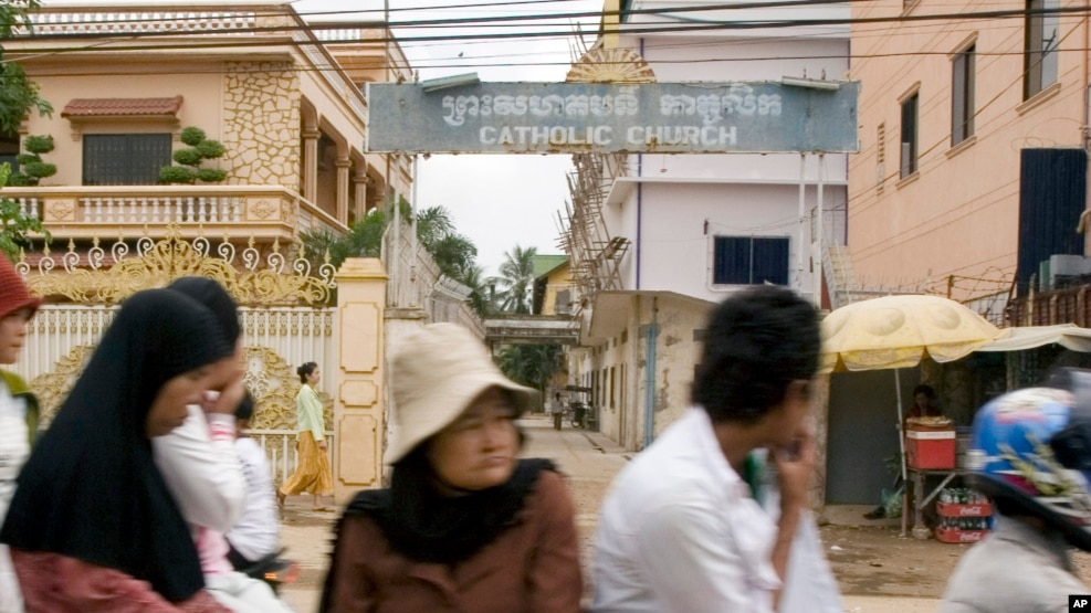 Cambodians and Muslims ride on a motor-cart past a catholic church in Phnom Penh, Cambodia, Tuesday, July 17, 2007. 