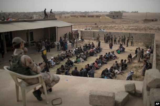 FILE - Displaced people who fled from Islamic State-held territory sit outside a mosque guarded by Iraqi soldiers in Shuwayrah, south of Mosul, Iraq, Nov. 1, 2016.