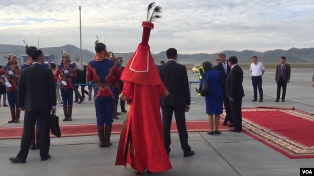 A Mongolian woman dressed in red traditional deel with LV shoes greets US Secretary of State John Kerry as her arrives in Ulaanbaatar, Mongolia. (N. Ching/VOA)