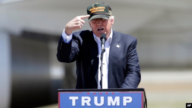 Republican presidential candidate Donald Trump gestures to a his camouflaged "Make America Great" hat as he discuses his support by the National Rifle Association at a campaign rally at the Redding Municipal Airport, June 3, 2016, in Redding, California.