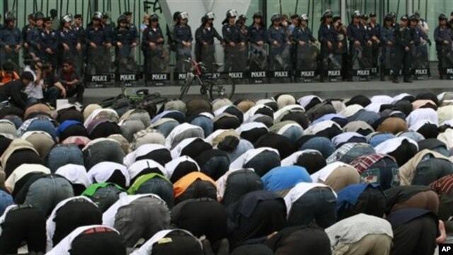 Thai police officers look at Thai-Muslim demonstrators conducting afternoon prayers outside a shopping mall where the office of Google Thailand is located, during a demonstration against a video produced in the United States that denigrates the Prophet Mu