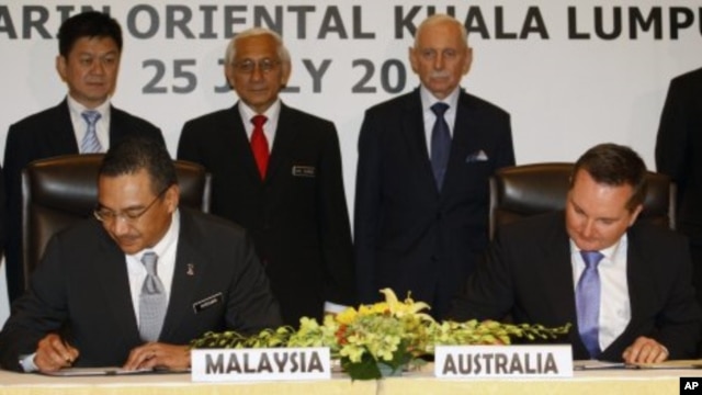 Malaysian Home Minister Hishammuddin Hussein, foreground left, and Australian Immigration Minister Chris Bowen, foreground right, sign documents to swap refugees between the two countries, in Kuala Lumpur, Malaysia, July 25, 2011