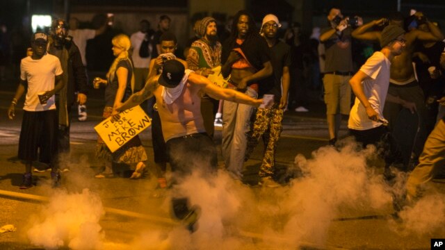 A protester kicks a tear gas canister back towards police after protests in reaction to the shooting of Michael Brown turned violent near Ferguson, Missouri, August 17, 2014.